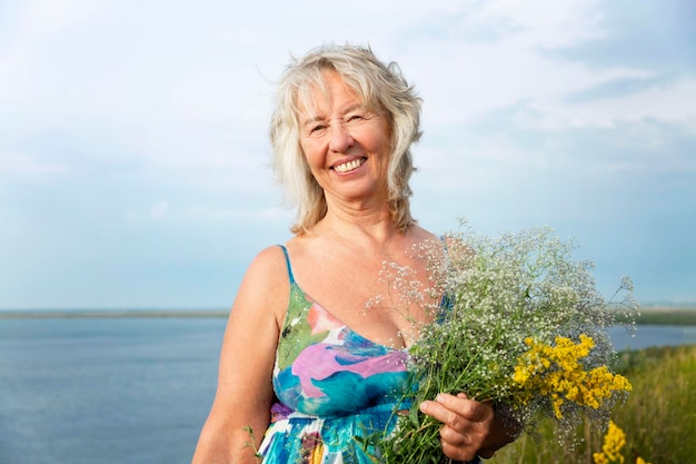 자연과 휴식에 대한 필드 사랑에 꽃을 들고 여름 sundress에 웃는 노인 여성