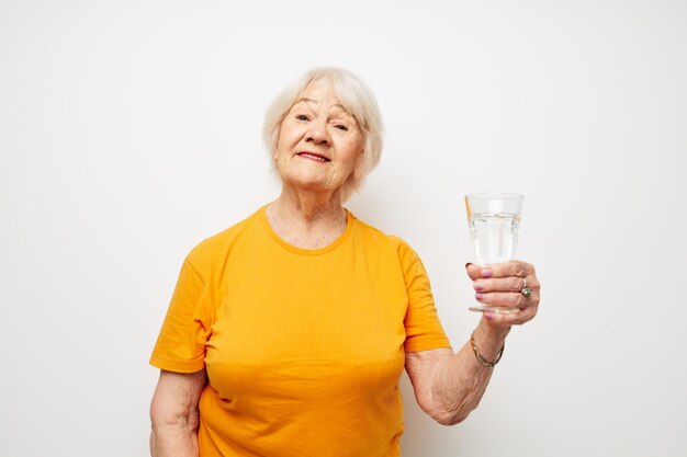 Smiling elderly woman in yellow tshirts a glass of water in his hands cropped view