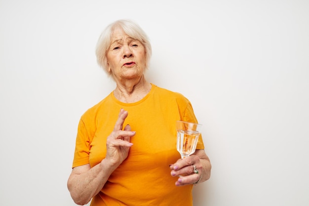 Smiling elderly woman in yellow tshirts a glass of water in his hands cropped view