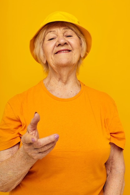 Smiling elderly woman in yellow tshirts hat posing isolated background high quality photo