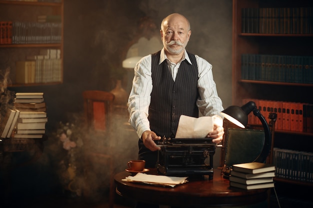 Smiling elderly writer works on retro typewriter