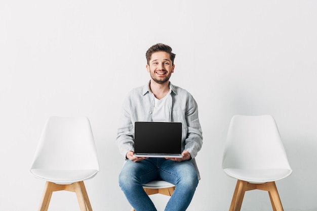 Smiling employee looking at camera while holding laptop with blank screen on chair