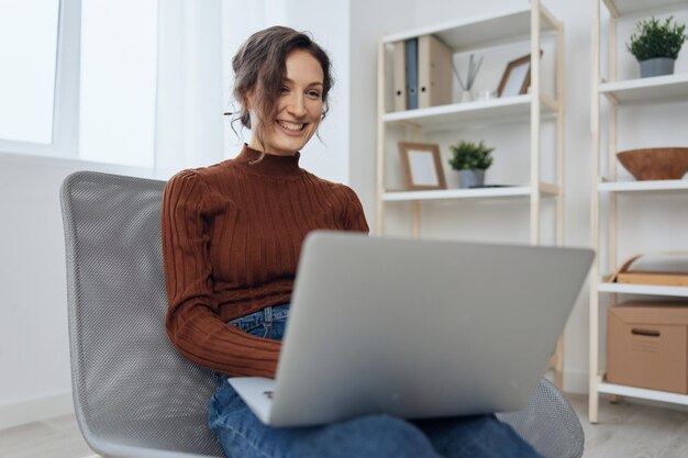 Smiling enjoyed conversation in video call conference with\
boyfriend cheerful curly woman sit in chair with laptop on knees at\
home distance remote communication concept copy space for ad