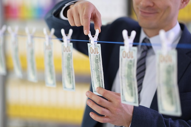 Smiling entrepreneur hangs dollar bills to dry on clothesline in hallway dishonest businessman