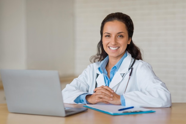 Smiling european doctor at desk with laptop and notes