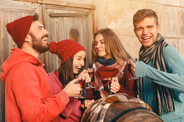 Smiling european men and women during party photoshoot. The guys posing as friends at studio fest with wineglasses with hot mulled wine on foreground.