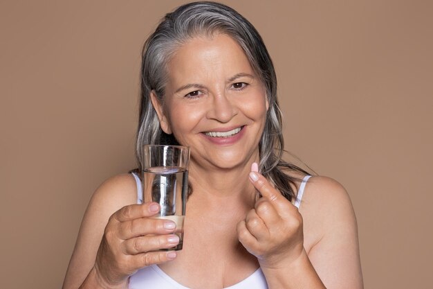 Foto la donna dai capelli grigi senior europea sorridente prende le vitamine e tiene il bicchiere d'acqua