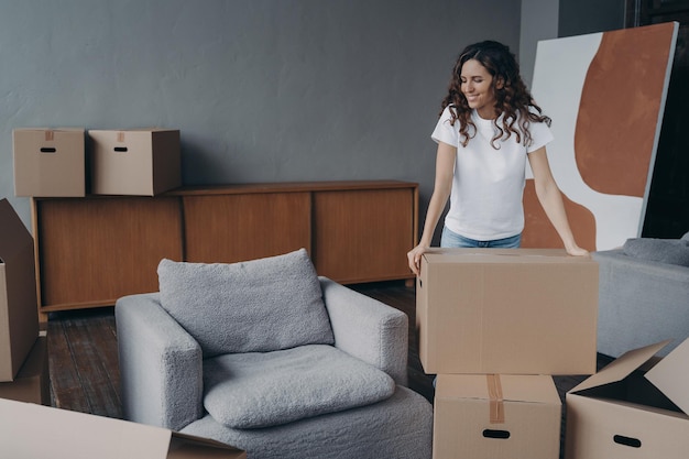 Smiling european woman is packing things Young lady is unpacking cardboard boxes in new apartment