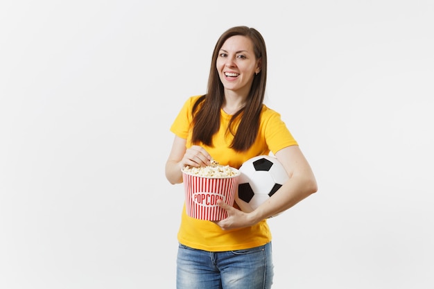 Улыбающаяся европейская молодая женщина, футбольный фанат или игрок в желтой форме держит футбольный мяч, ведро попкорна на белом фоне. Спорт, играть в футбол, приветствовать, концепция образа жизни людей болельщиков.