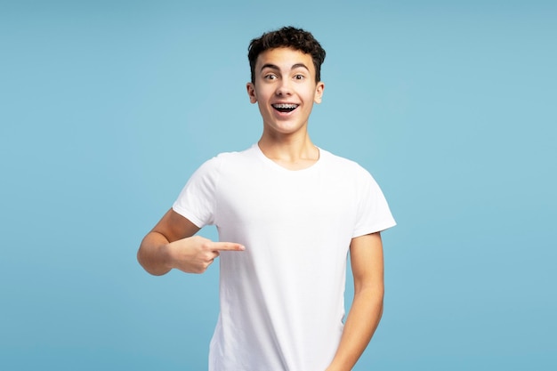 Smiling excited boy wearing white t shirt pointing finger at her mockup looking at camera