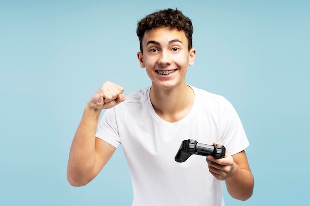 Smiling excited boy winner holding console using joystick playing video games looking at camera