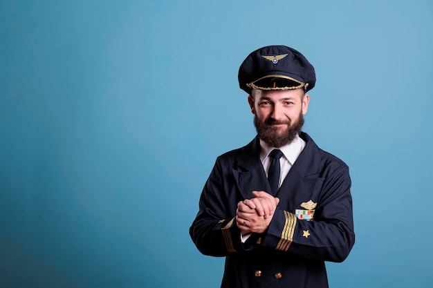 Smiling excited plane aviator in professional uniform clapping\
hands. happy positive airlane pilot applauding, shaking palms,\
standing, looking at camera, studio medium shot