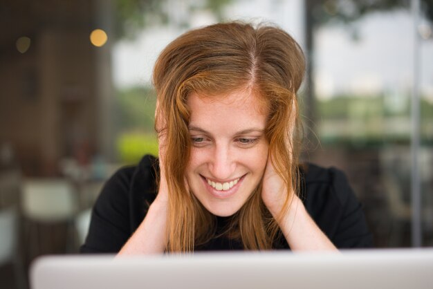 Donna eccitata sorridente che esamina lo schermo del computer portatile