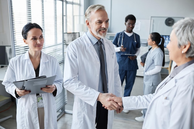 Photo smiling experienced hospital worker shaking hand of mature female colleague