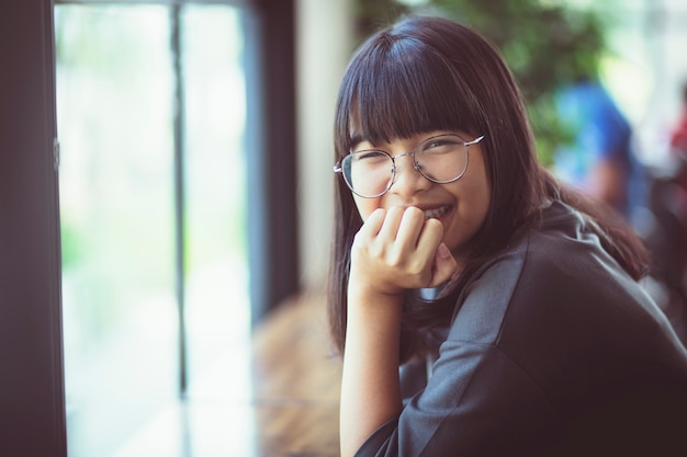 Photo smiling face of asian teenager sitting beside home window