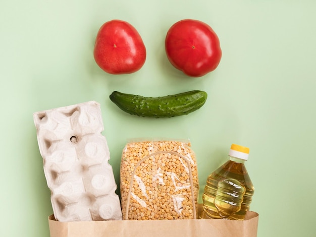 Foto faccia sorridente fatta di pomodori e cetrioli su sacchetto di carta con cibo su sfondo verde