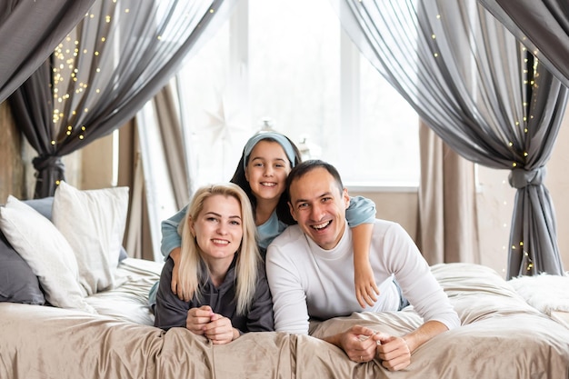 La famiglia sorridente si trova su un letto bianco.