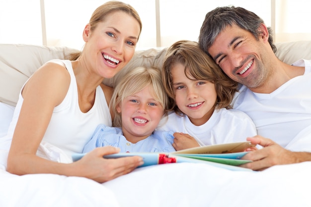 Famiglia sorridente che legge un libro sul letto