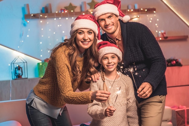 Photo smiling family in santa hats celebrating new year with sparklers