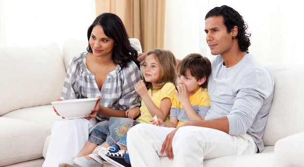 Улыбающаяся семья смотрит телевизор на диване