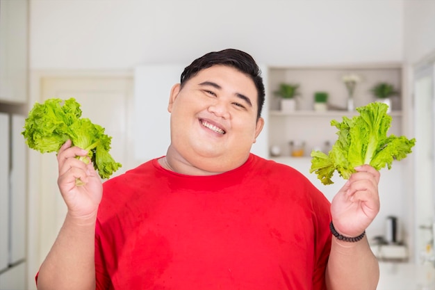 Smiling fat man holds organic lettuce in the kitchen