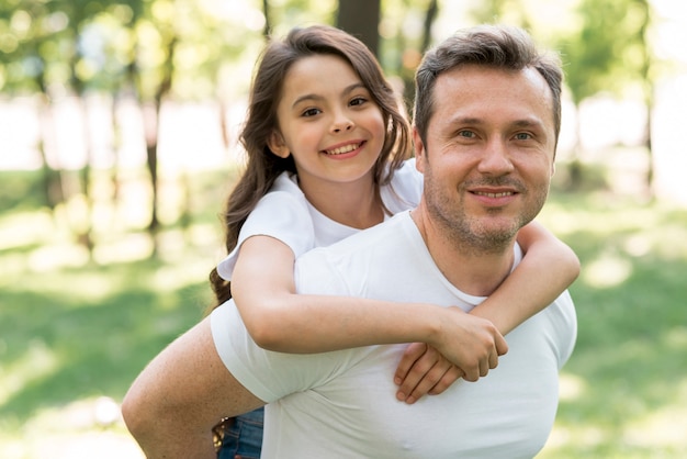 Foto sorridente padre piggybacking sua figlia carina al parco