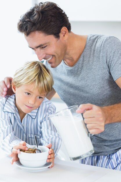 Smiling father pouring milk for sons cereal