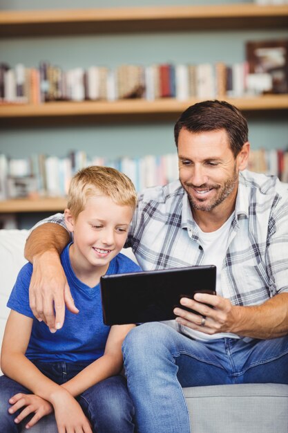 Smiling father and son using digital tablet while sitting on sofa