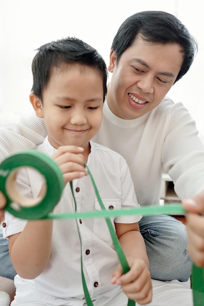 Smiling father and sonn decorating christmas and new year presents with green ribbon