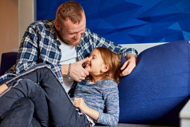 Smiling father with daughter having fun, tickle at sofa in living room, at home. Happy family.