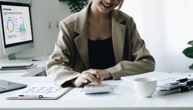 Smiling female accountant using calculator while sitting at office desk with digital tablet and financial documents