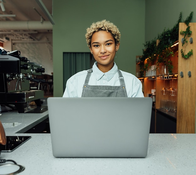 カフェでデジタル タブレットと笑顔の女性バリスタ コーヒー ショップのカウンターでエプロンを着た若い女性の肖像画