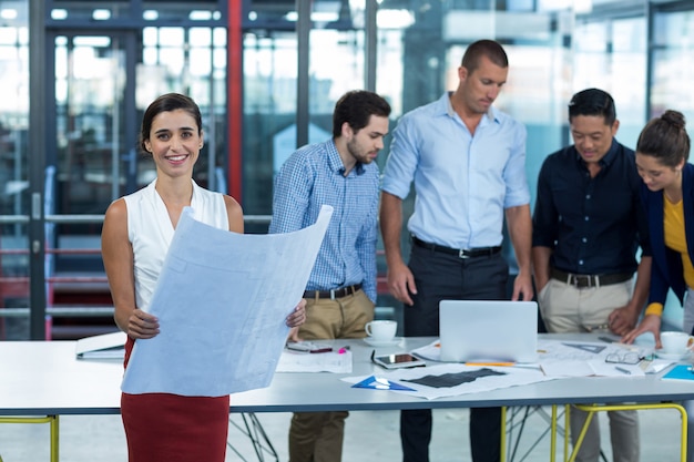 Smiling female business executive holding blueprint in office