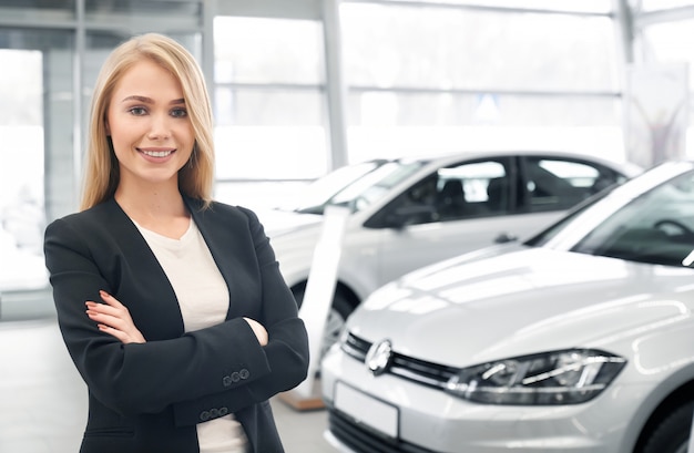 Smiling female car dealer posing in front of new automobiles