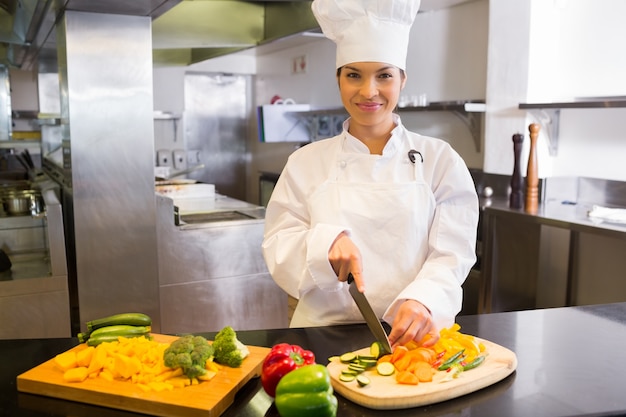 Smiling female chef cutting vegetables in kitchen