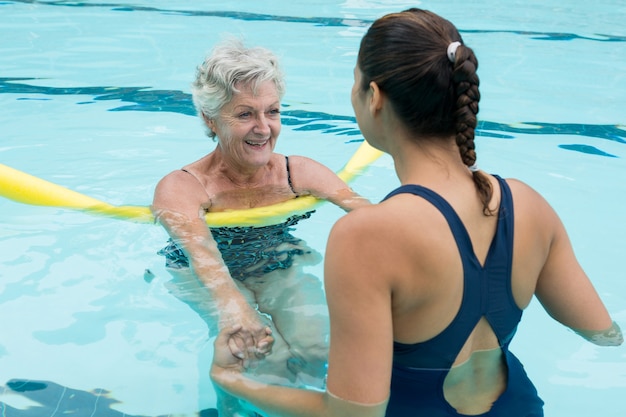 Smiling female coach helping senior woman in swimming pool