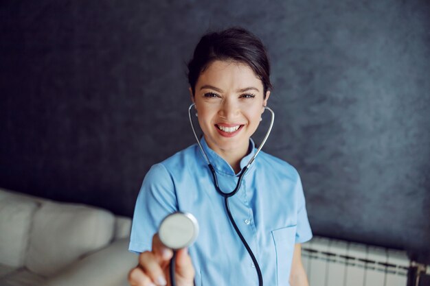 Medico femminile sorridente che tiene lo stetoscopio verso la telecamera come se stesse esaminando i polmoni