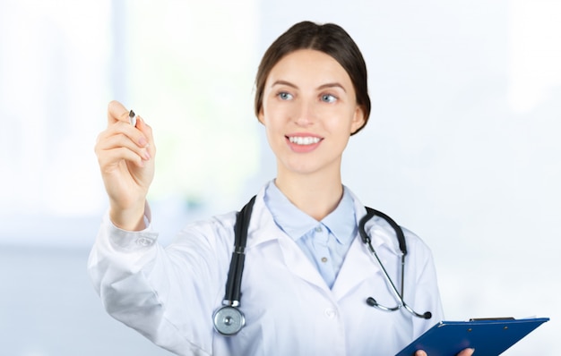 Smiling female doctor in white coat with stethoscope and clipboard pointing finger