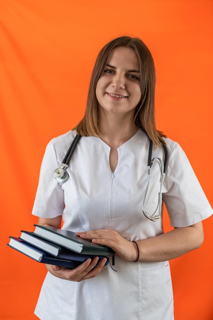 Smiling female doctor with stethoscope and books in hands posing isolated on plain background