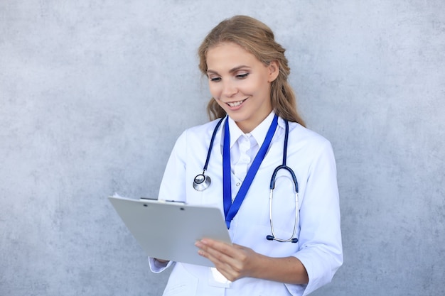 회색 배경 위에 격리된 건강 카드를 들고 청진기를 들고 웃고 있는 여성 의사.