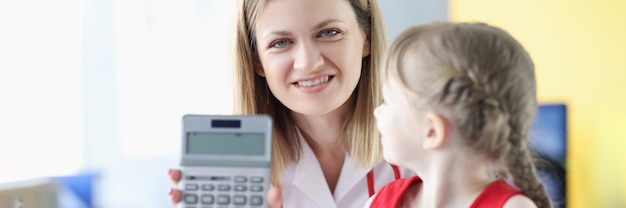 Smiling female doctor with young girl holding calculator. Medical insurance concept