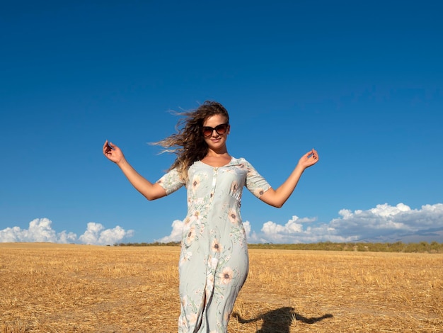 Smiling female in dress spreading arms in field