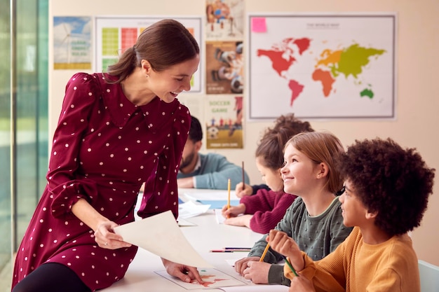 Photo smiling female elementary school teacher working at desk in classroom with students