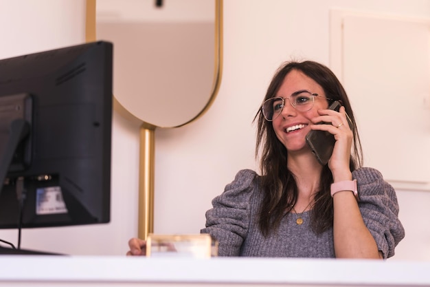 Улыбающаяся работница звонит по телефону во время работы на компьютере в офисе