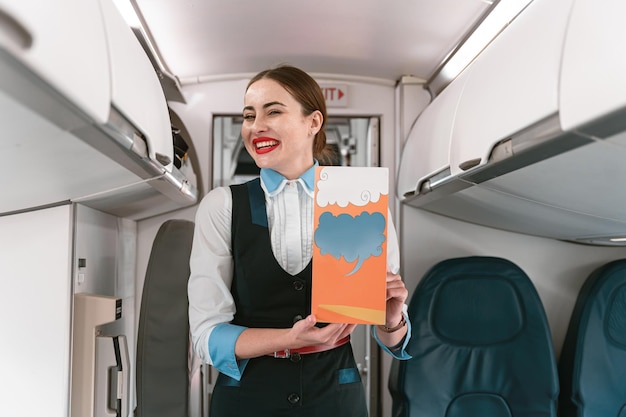 Smiling Female flight attendant holding instruction booklet before flight