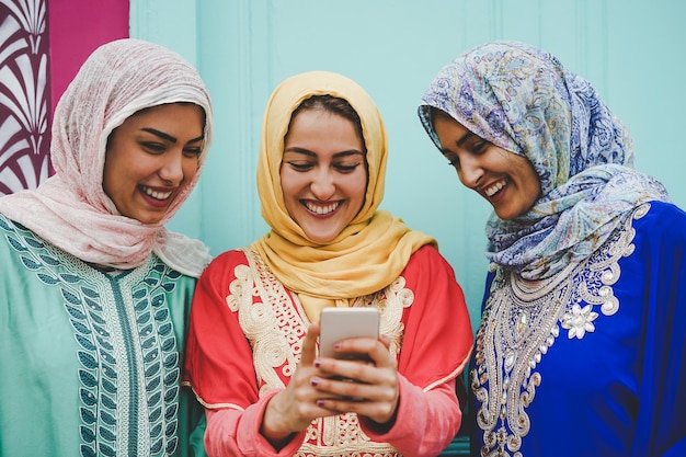 smiling female friends using smart phone against wall