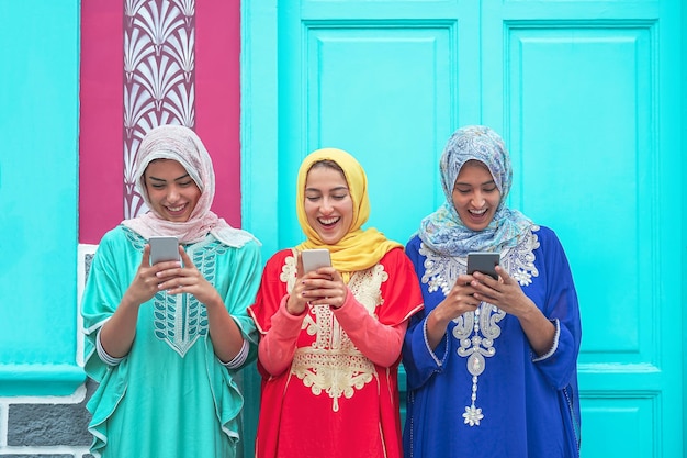 Photo smiling female friends using smart phones against building