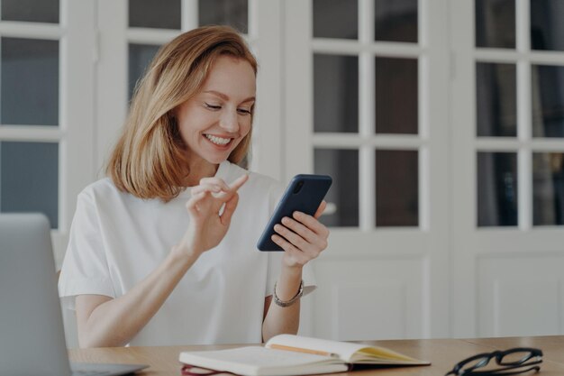 Smiling female holding smartphone using mobile apps browsing the Internet in the workplace