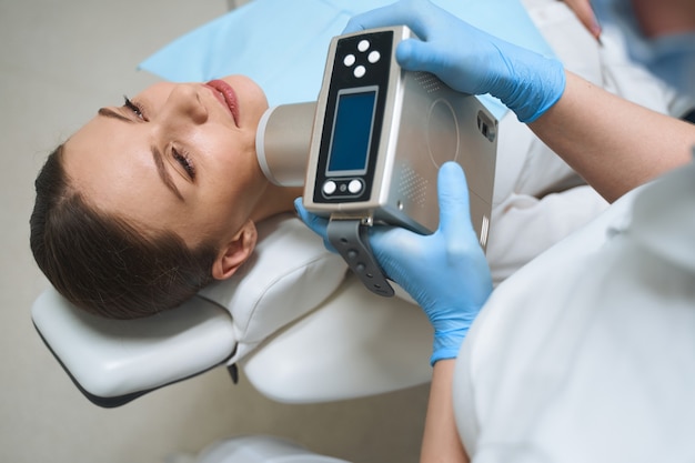 Smiling female is lying in chair and enjoying teeth treatment with electronical machine in modern clinic