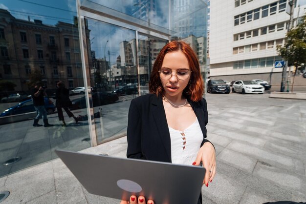 Фото Улыбающаяся женщина смотрит на свой ноутбук на открытом воздухе, современный образ жизни